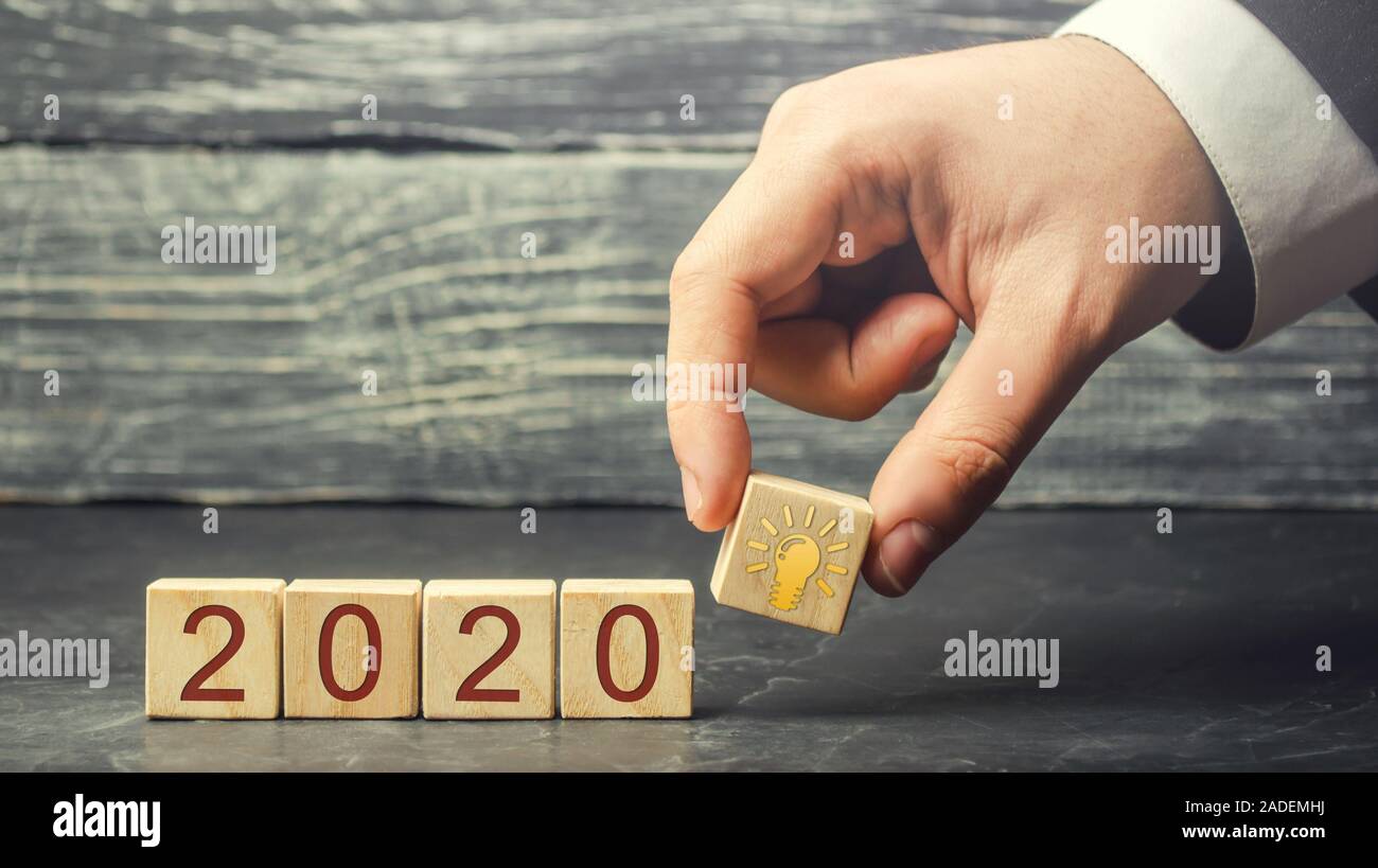 Businessman puts wooden blocks 2020 with an idea light bulb. Business planning and strategy. Innovative ideas. Action plan. Stock Photo
