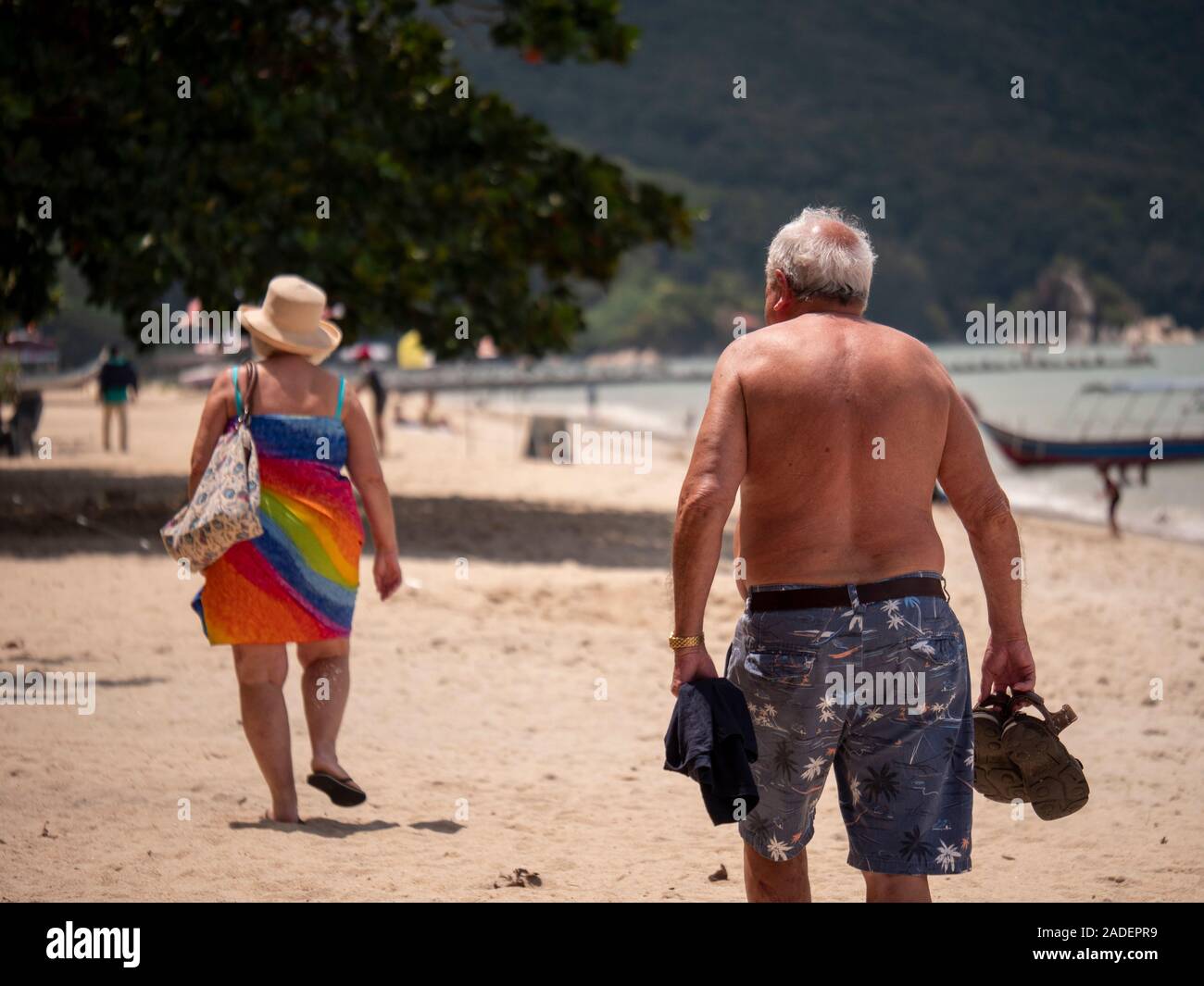 Old couple walking swimsuit in sandy beach coast line whaite sands green background Stock Photo