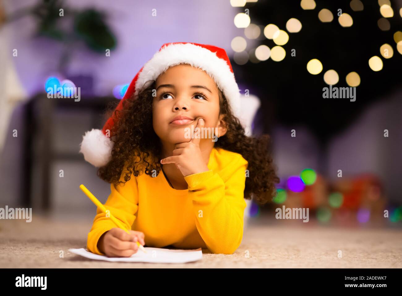 Wistful little afro girl thinking about letter to Santa Claus Stock Photo