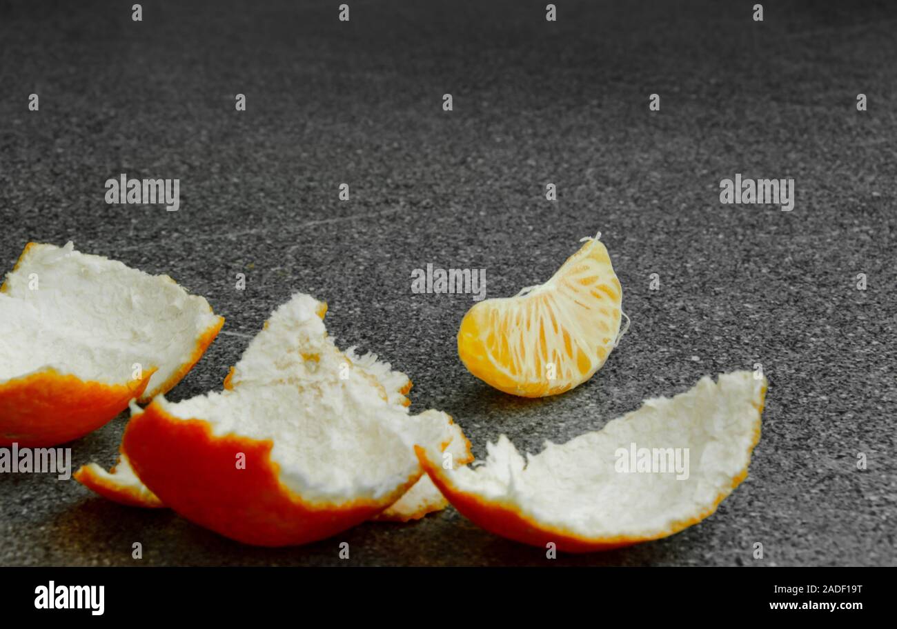 An orange light tangerine on a table, the paring is peeled and one slice lays on the table Stock Photo