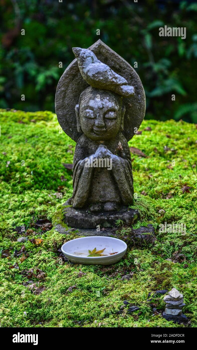 Stone statues of smiling Jizo Bosatsu with green moss at zen garden in