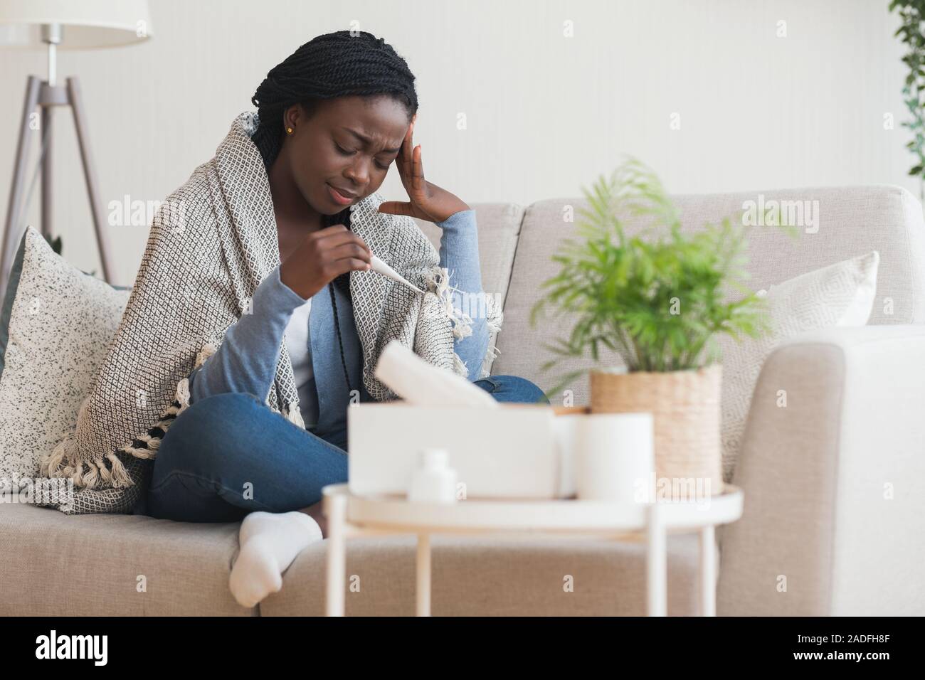 Sick black girl sitting on sofa with thermometer Stock Photo