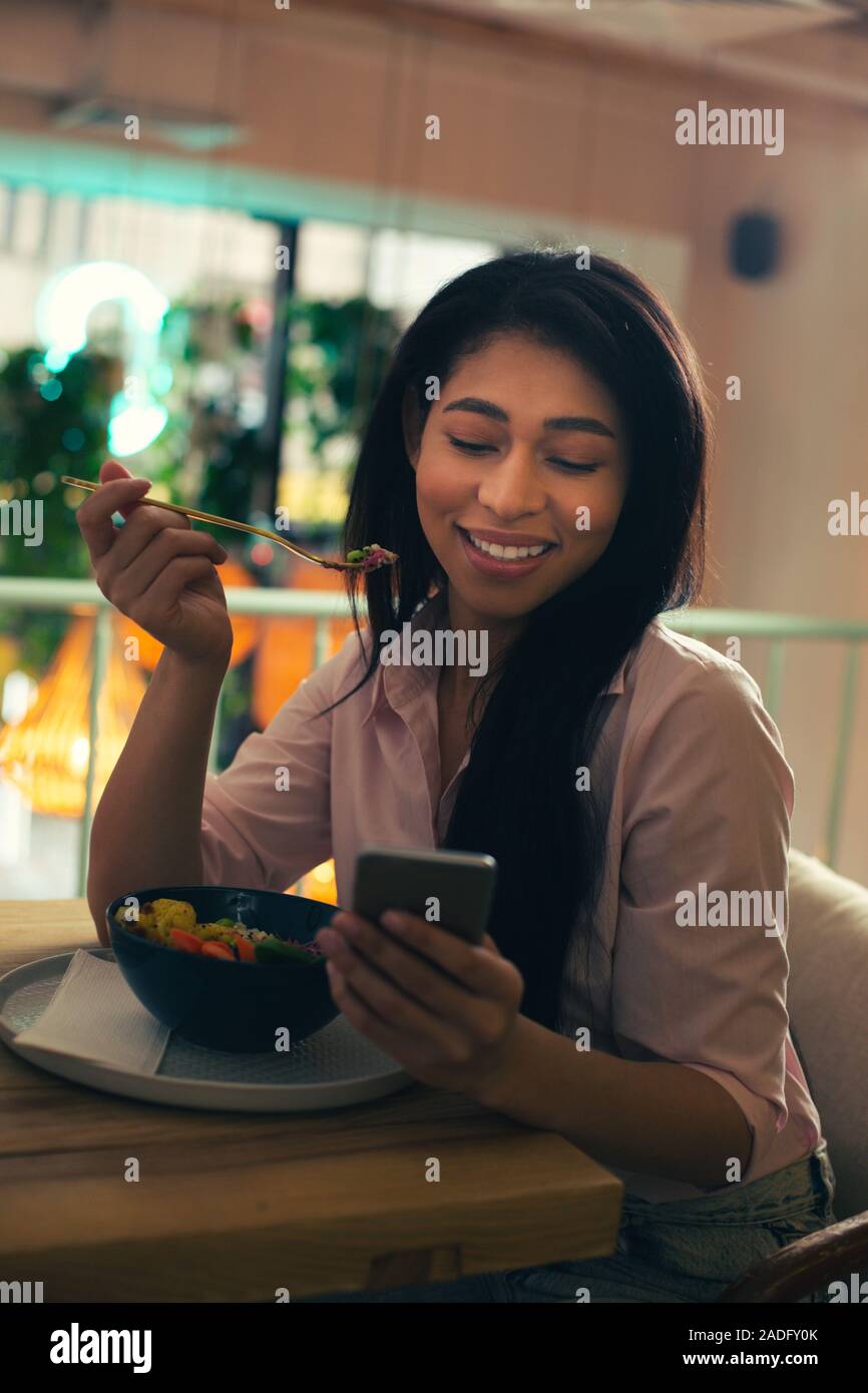 Smiling lady using her smartphone while eating lunch Stock Photo