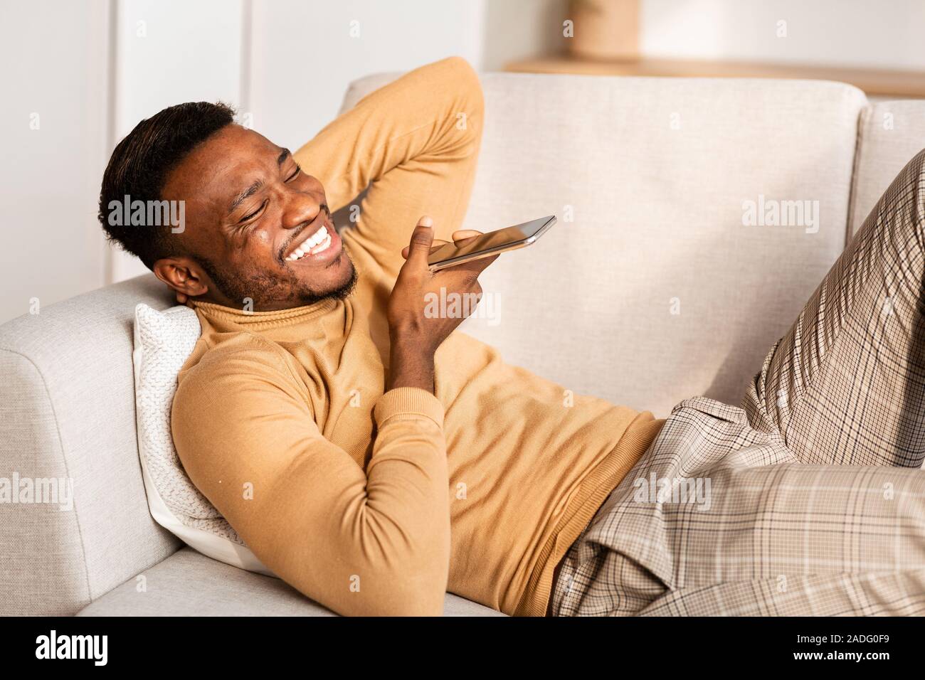 Man Using Phone Voice Assistant Lying On Couch At Home Stock Photo