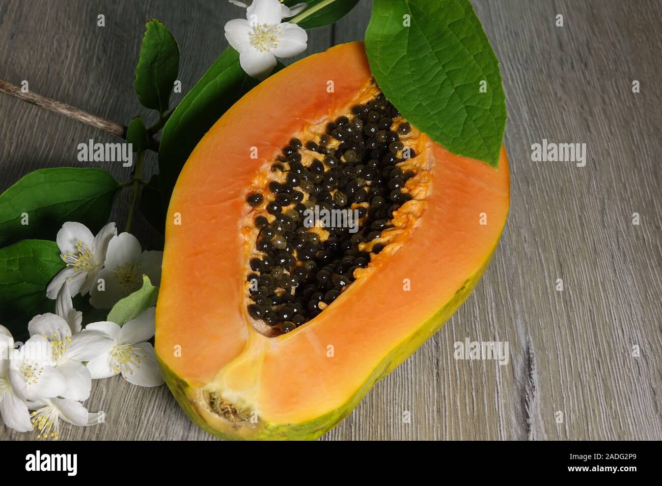 Fresh sliced papaya with seeds inside on a wooden background with jasmine flowers. Half of