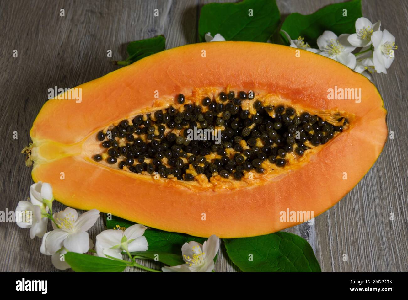 Fresh sliced papaya with seeds inside on a wooden background with jasmine flowers. Half of
