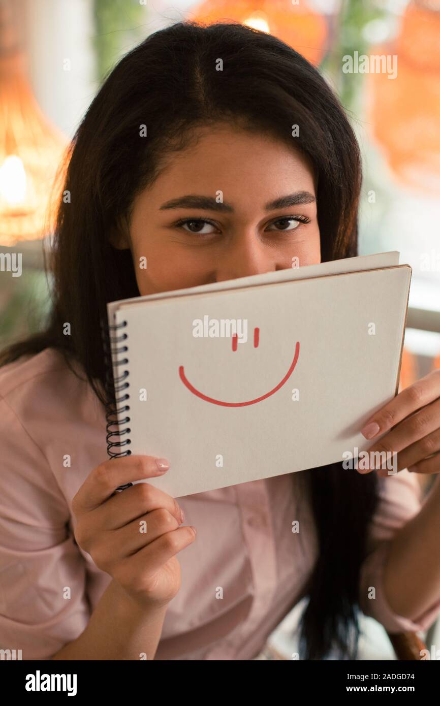 Dark haired woman hiding behind the drawn smile Stock Photo