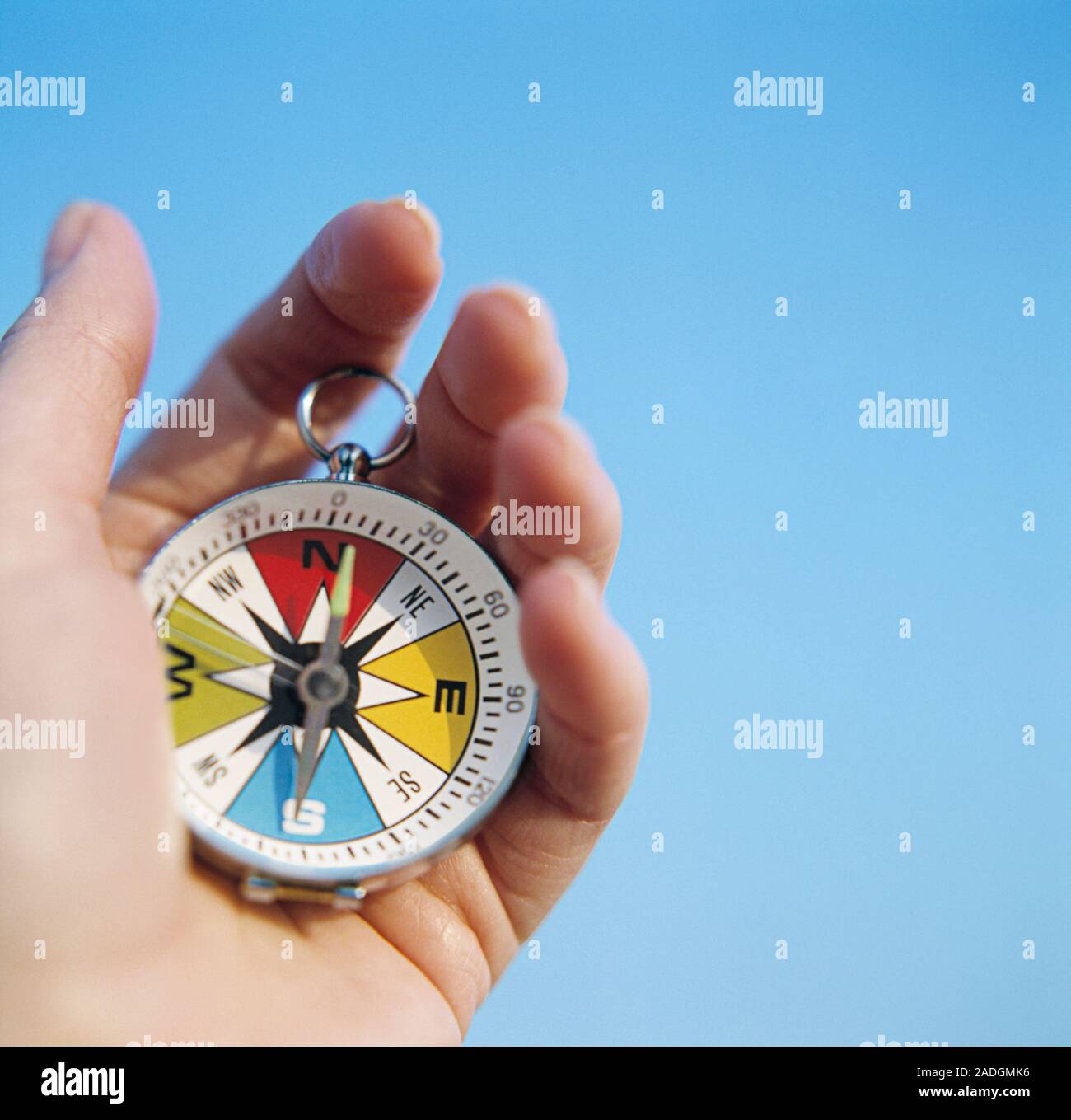 Magnetic compass. Hand holding a compass against a blue sky. The compass has a free-swinging magnetised needle, which is seen pointing to North on the Stock Photo