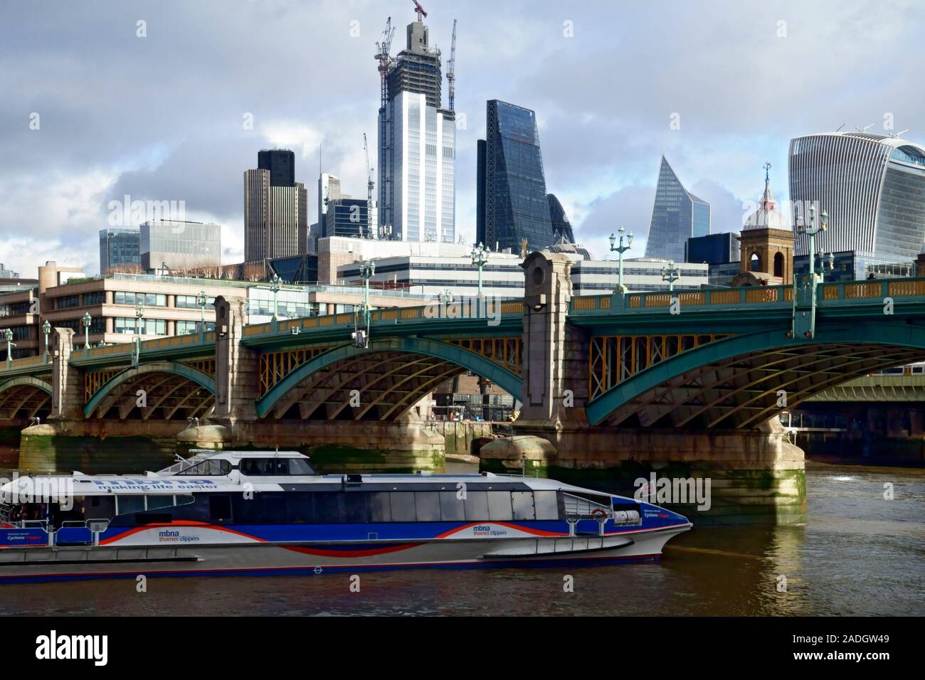 River cruise boat going under Southwark Bridge over the River Thames with the modern architecture of Londons iconic buildings Stock Photo