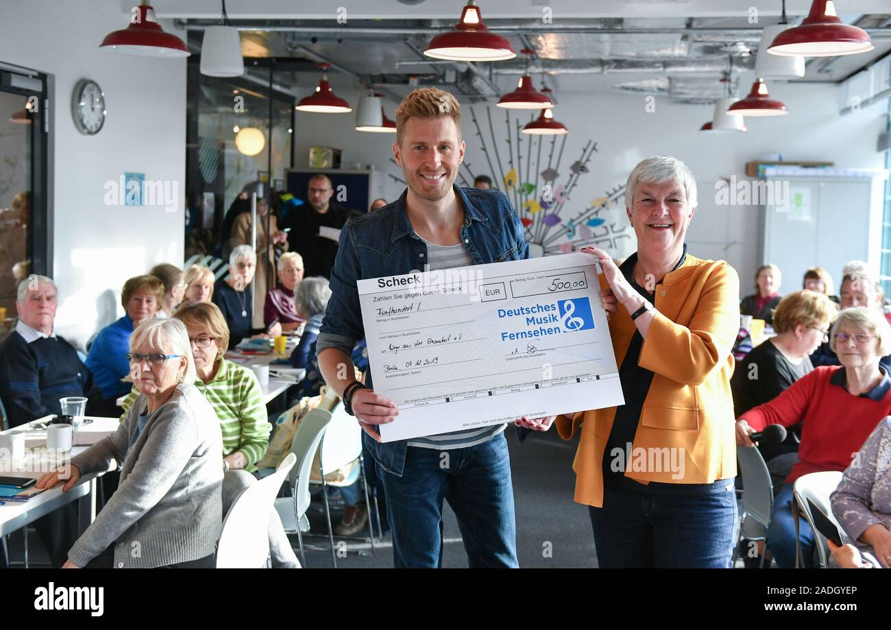 Berlin, Germany. 04th Dec, 2019. TV presenter Maximilian Arland visits senior citizens in the 'Versilberer-Cafe' of the association 'Wege aus der Einsamkeit e.V.' and hands over to Dagmar Hirche, chairman of the association, a donation cheque of the channel 'Deutsches Musik Fernsehen', where he moderates the daily TV programme 'Das große Wunschkonzert'. He has been an ambassador of the association for many years, which offers training courses for senior citizens on the subject of 'digital media'. Credit: Jens Kalaene/dpa-Zentralbild/dpa/Alamy Live News Stock Photo