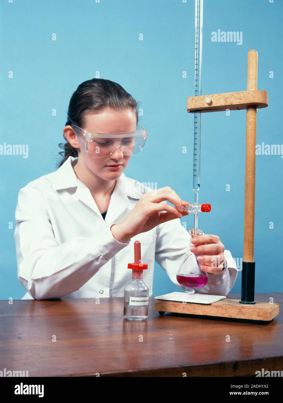 Titration experiment. Schoolgirl adding acid (from a burette) to