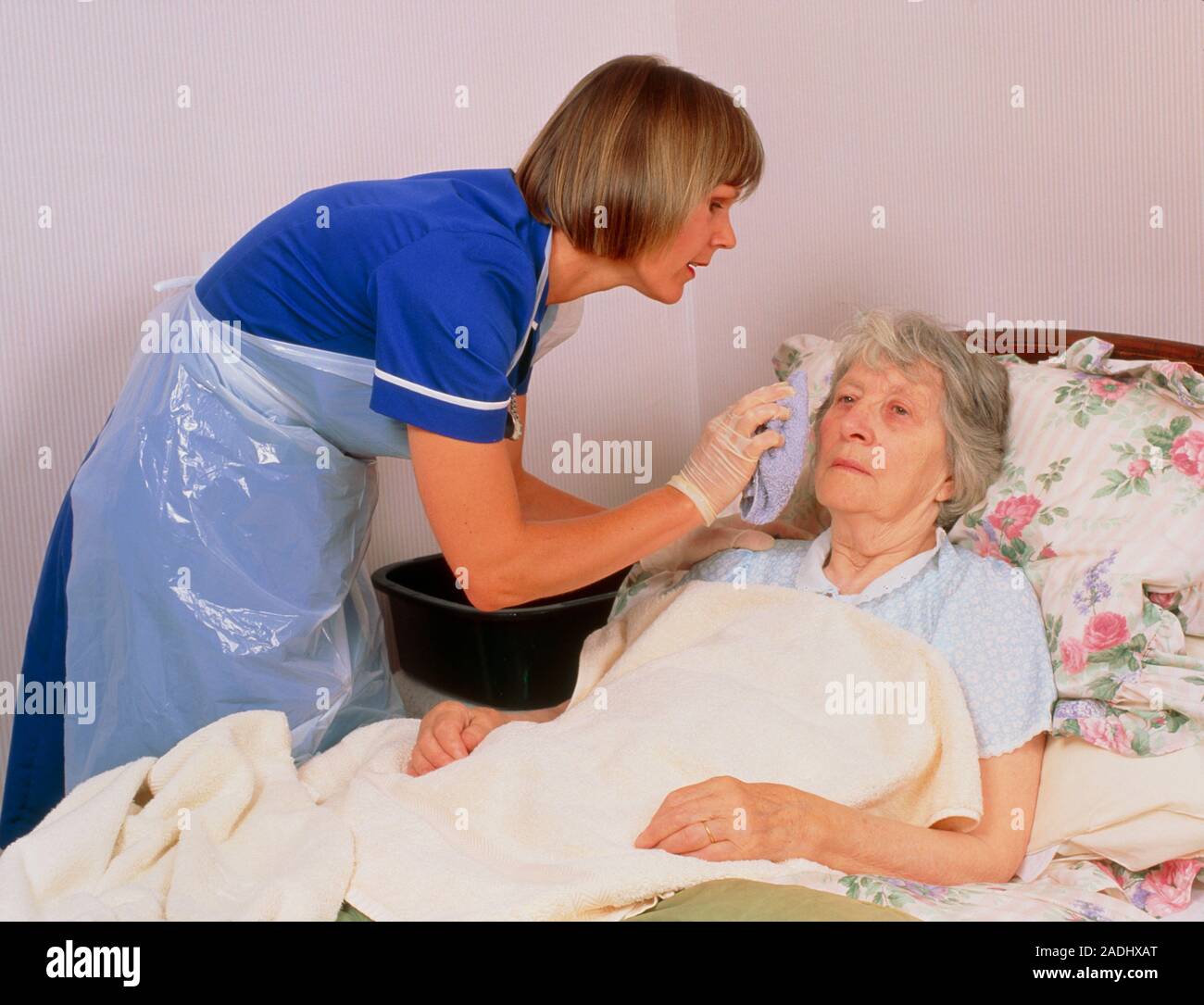 Bed bath. A district nurse gives an elderly bedridden woman a bed bath