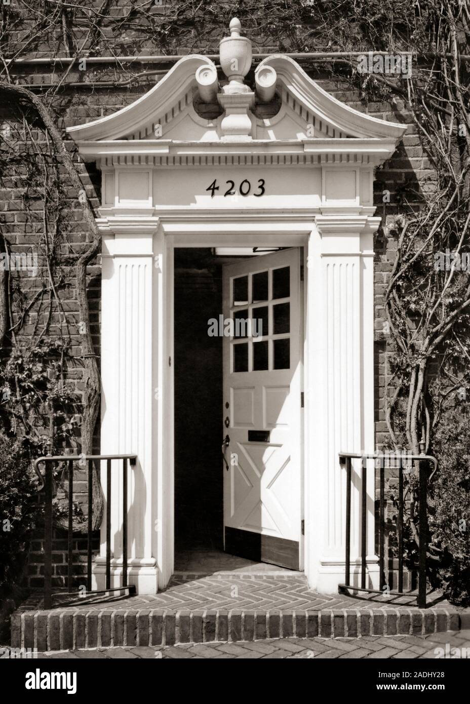 1960s OPEN FRONT DOOR WITH ARCHITECTURAL DETAIL OF BROKEN OR OPEN SWAN NECK PEDIMENT WITH URN - d5451 HAR001 HARS TYMPANUM BLACK AND WHITE HAR001 OLD FASHIONED URN Stock Photo