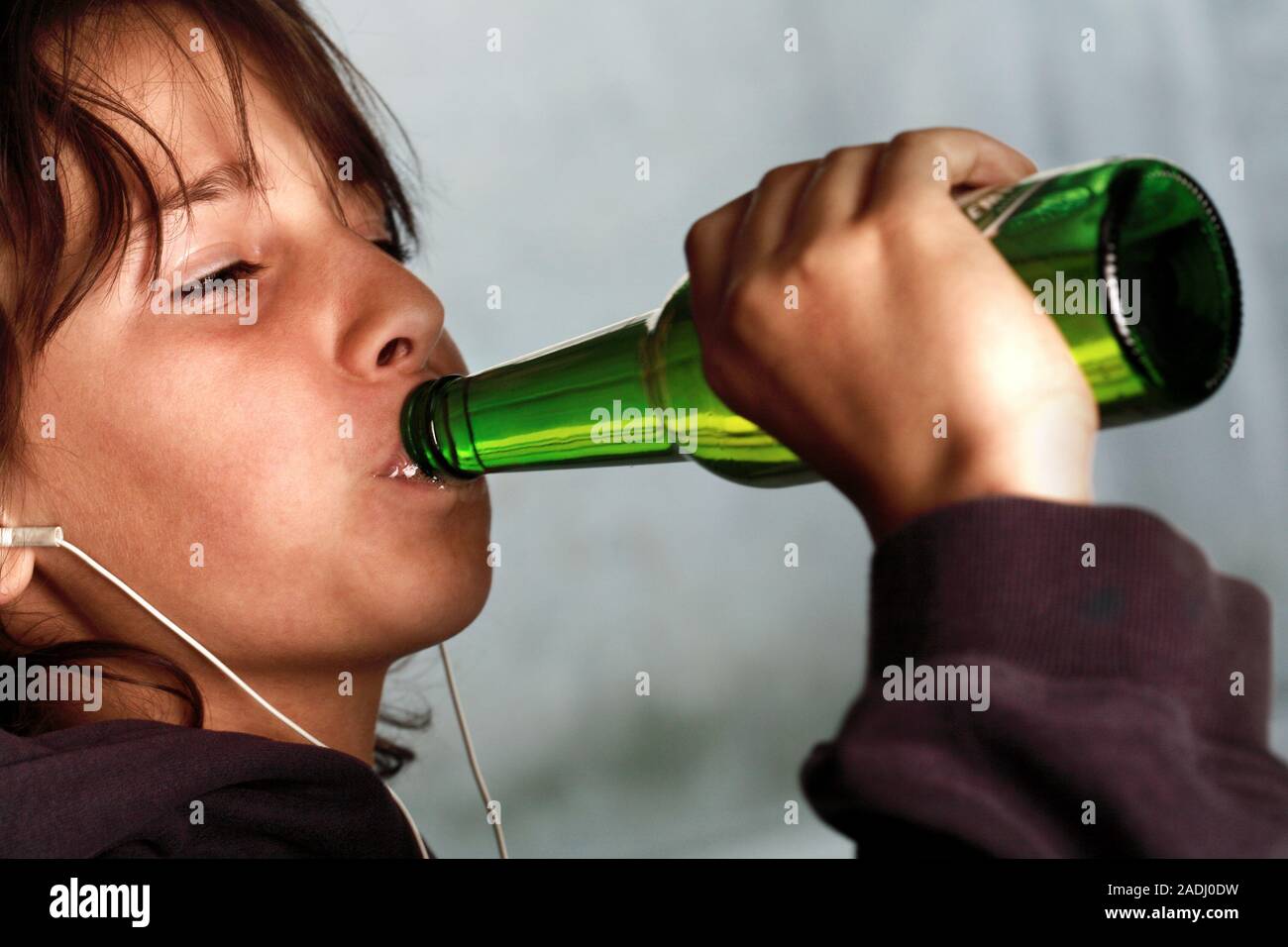 MODEL RELEASED. Underage drinking. Nine year old boy wearing headphones and drinking a bottle of beer. Stock Photo