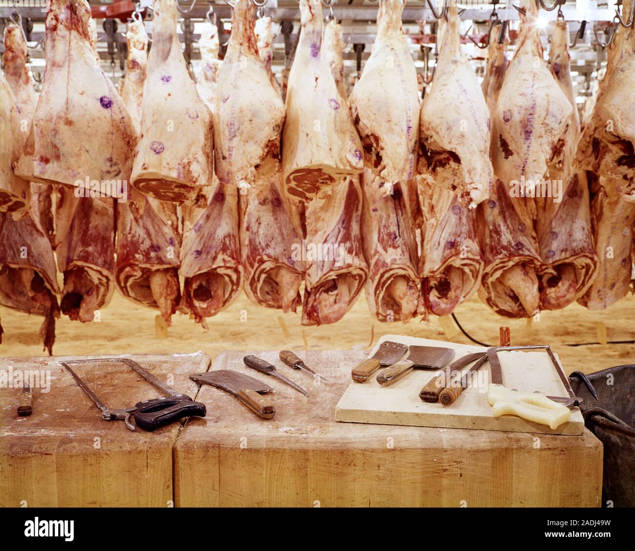 1970s BUTCHER’S TOOL ON CHOPPING BLOCK IN FRONT OF SIDE OF RAW DRESSED BEEF CARCASSES HANGING IN A WAREHOUSE MEAT COOLER - kf6221 HAR001 HARS FOOD PROCESSING HAR001 MEATS OLD FASHIONED WHOLESALE Stock Photo