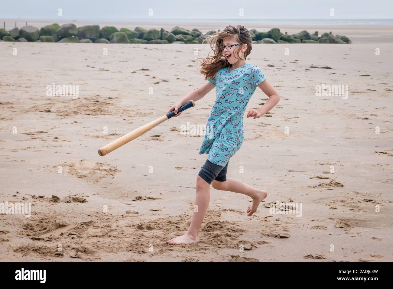 Girl on a family seaside holiday playing cricket with a baseball bat on