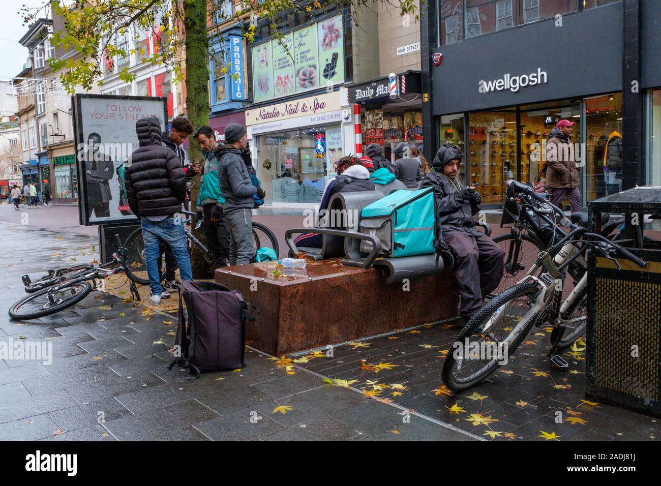Deliveroo couriers and other cyclists take a break on a wet day. Stock Photo