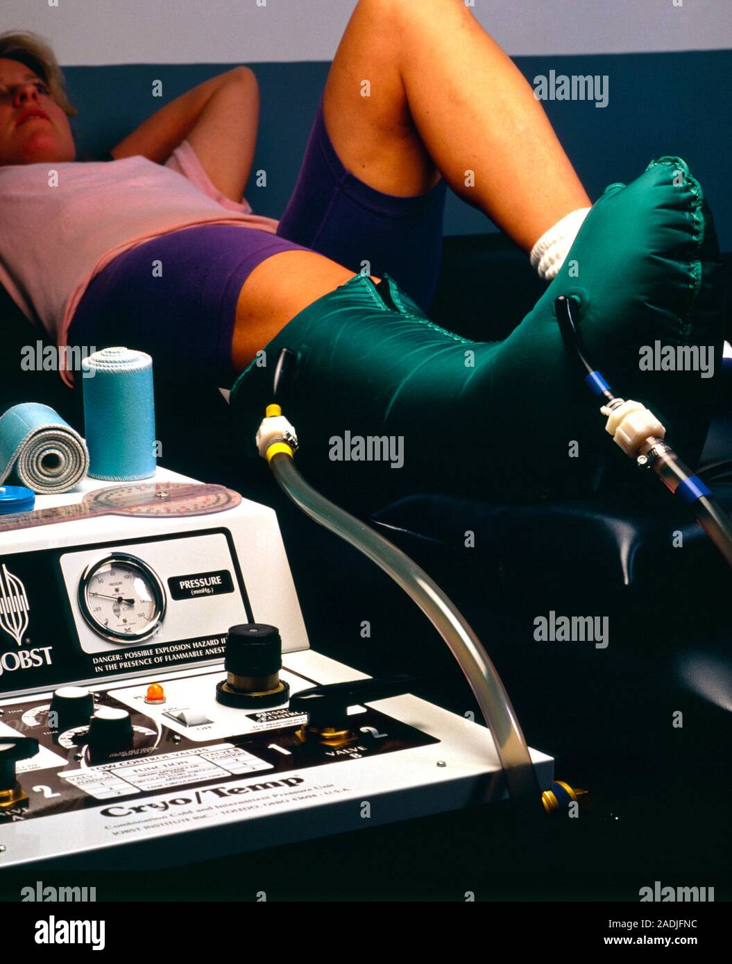 MODEL RELEASED. Cold treatment for sprained ankle. Woman lies on a bed with her foot inside a