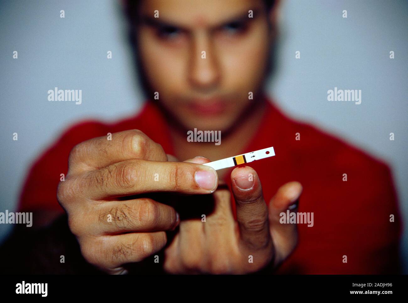 Blood glucose test. Man about to put blood from his pricked finger onto