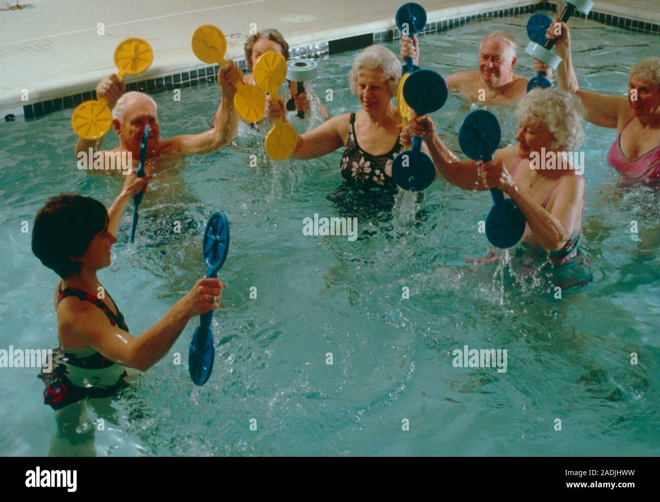 Water aerobics. Elderly people taking part in a water aerobics class. They are being instructed in stretching exercises by an aerobics instructor (low Stock Photo