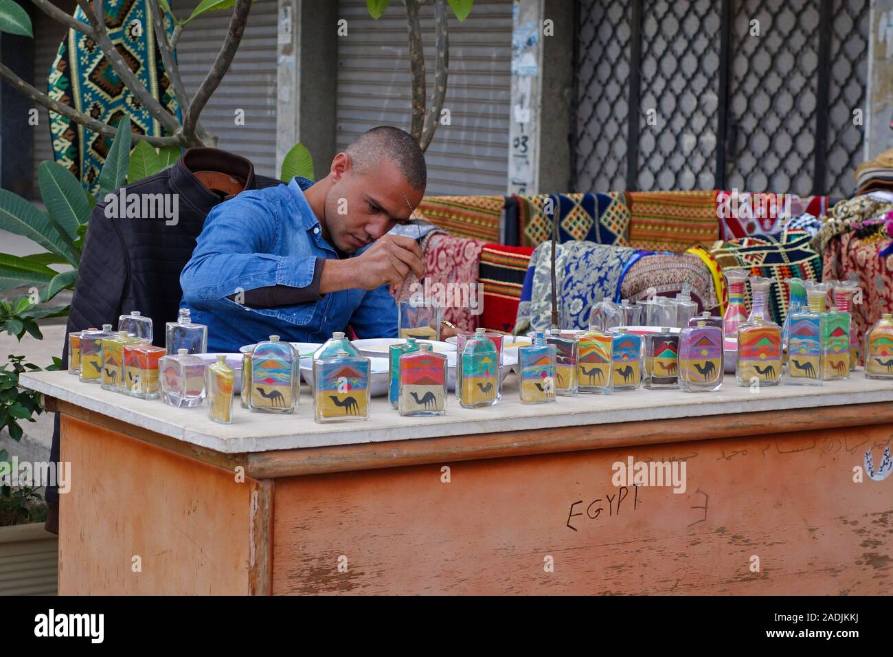 An Egyptian man making coloured sand sculptures in glass bottles or jars as souvenirs at Luxor, Egypt, Africa Stock Photo