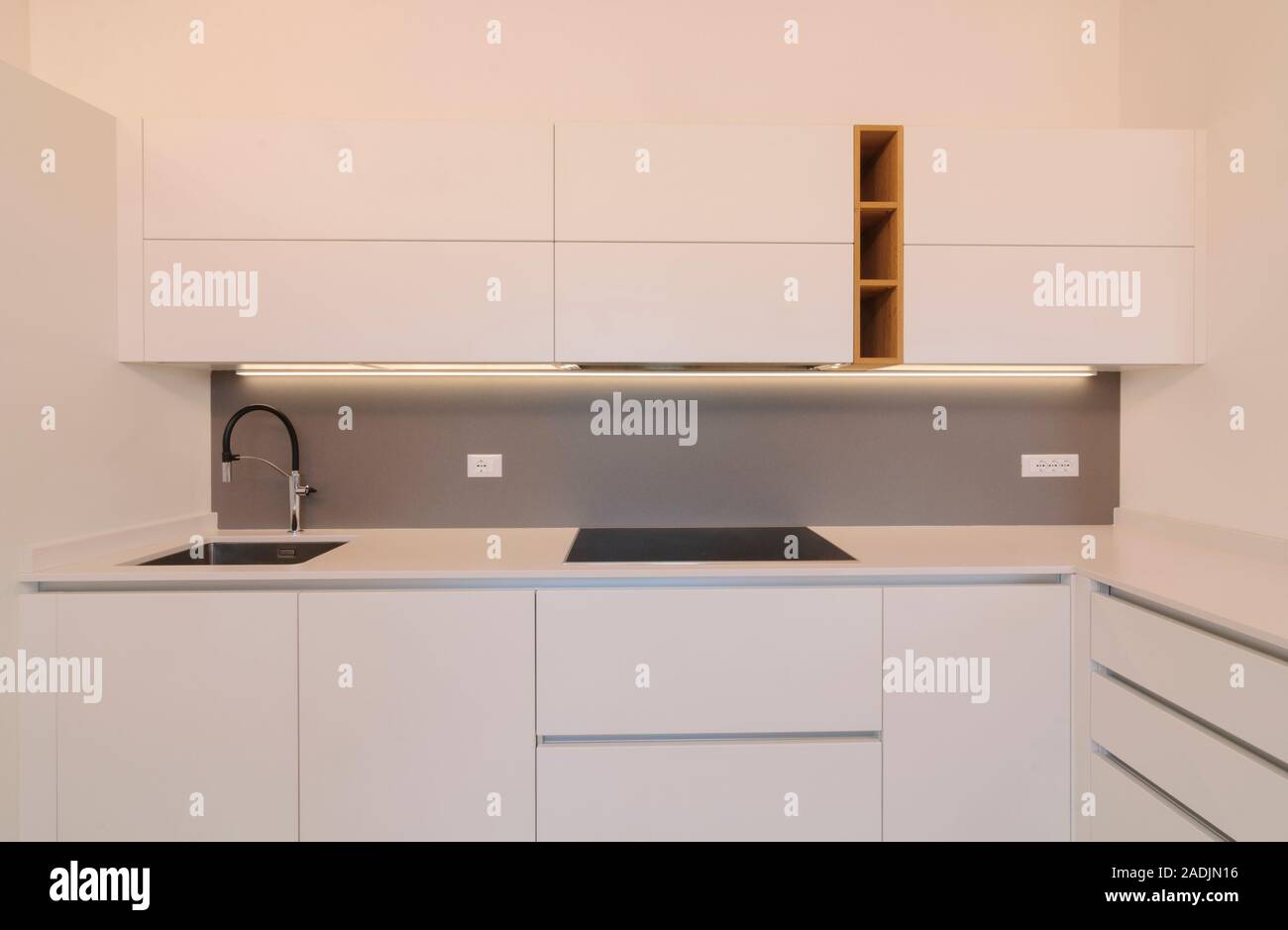 Modern and elegant kitchen interior with white cabinets, induction hob and wooden inserts. Contemporary Scandinavian style Stock Photo