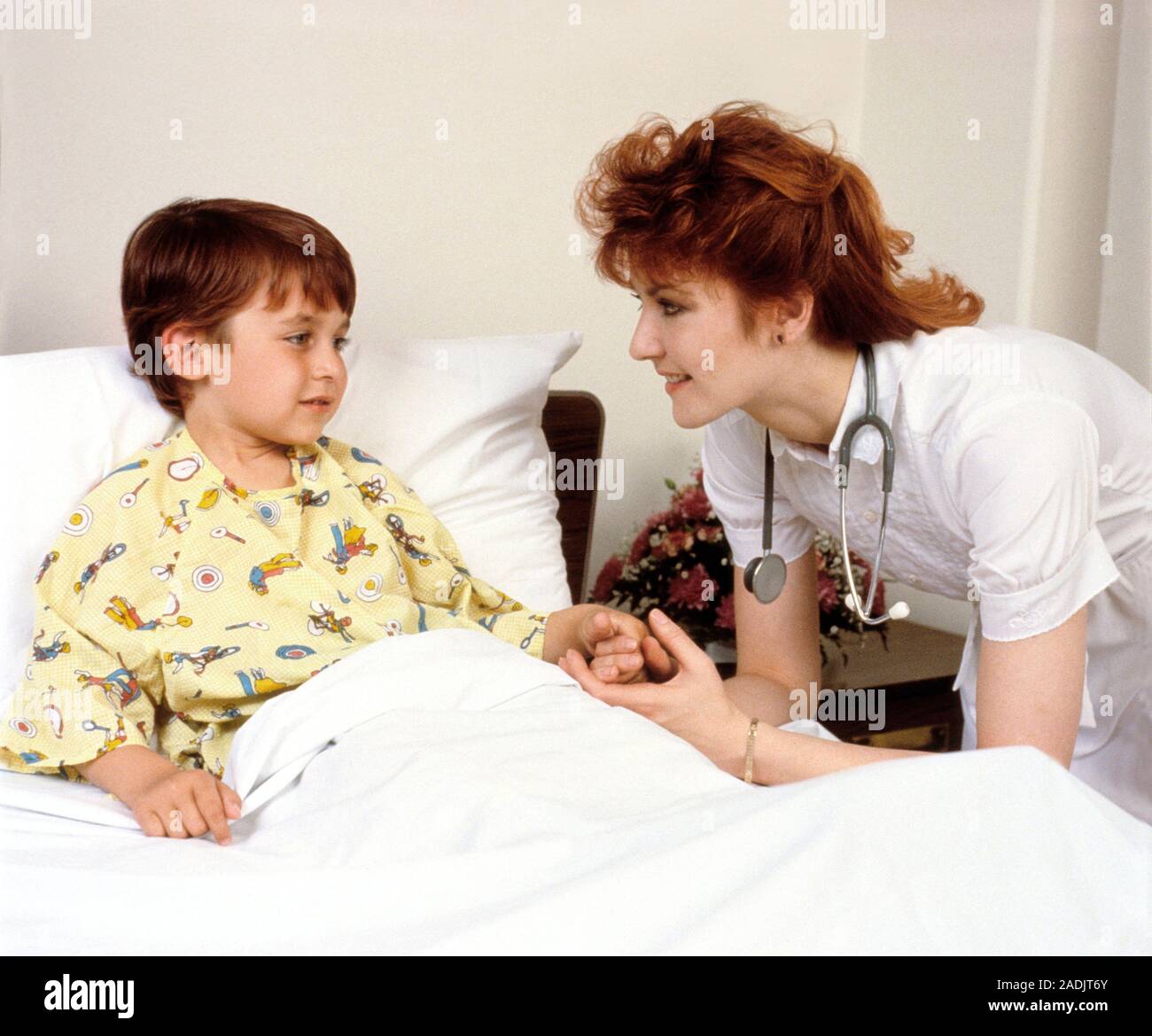 Paediatric care. Hospital nurse reassures a young boy sitting up in bed ...