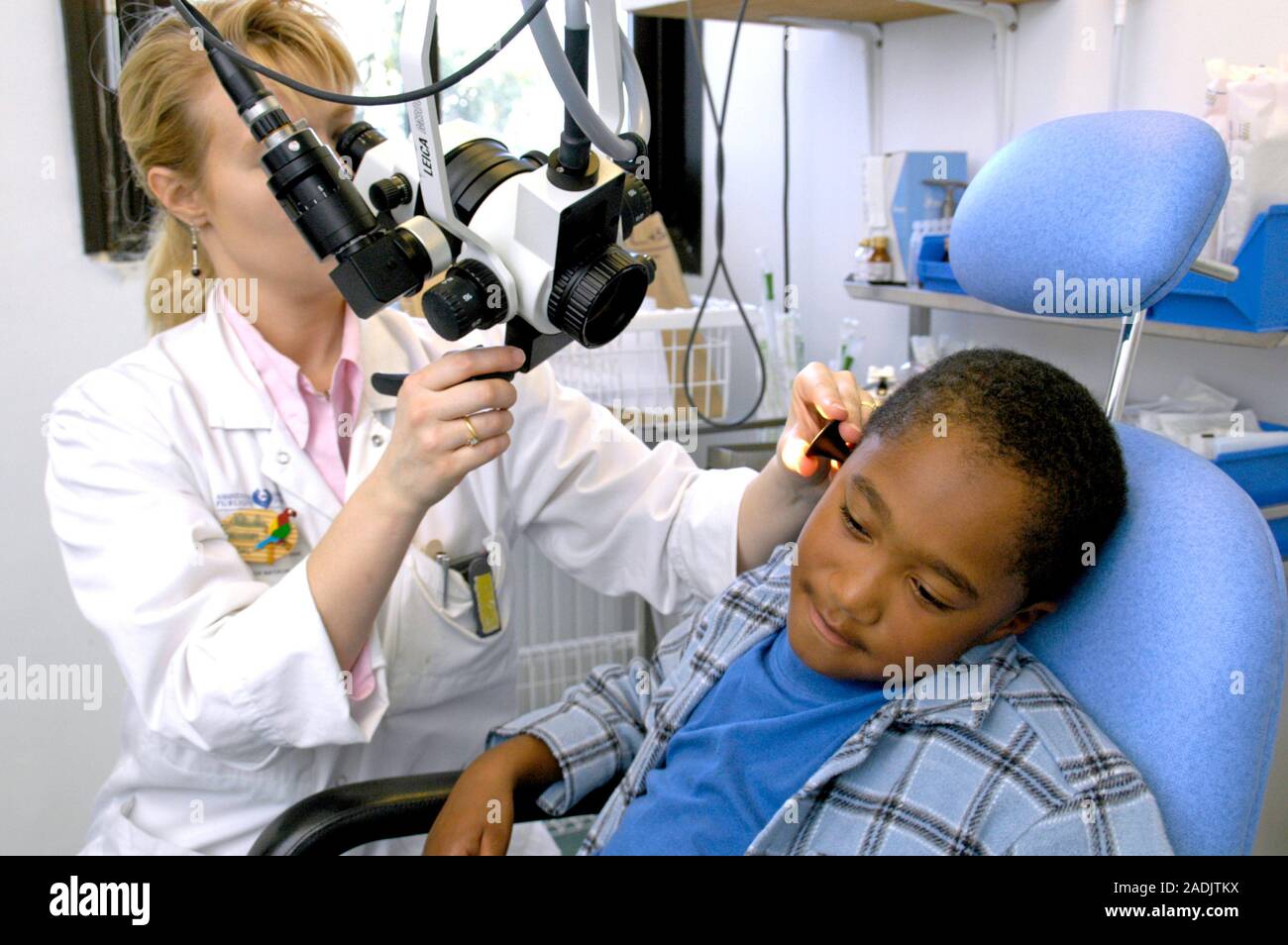 Ear examination. Doctor using a ceiling-mounted microscope to examine a ...