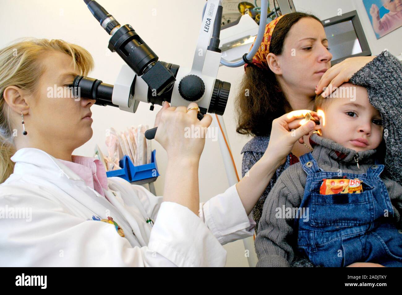Ear examination. Doctor using a ceiling-mounted microscope to examine a ...