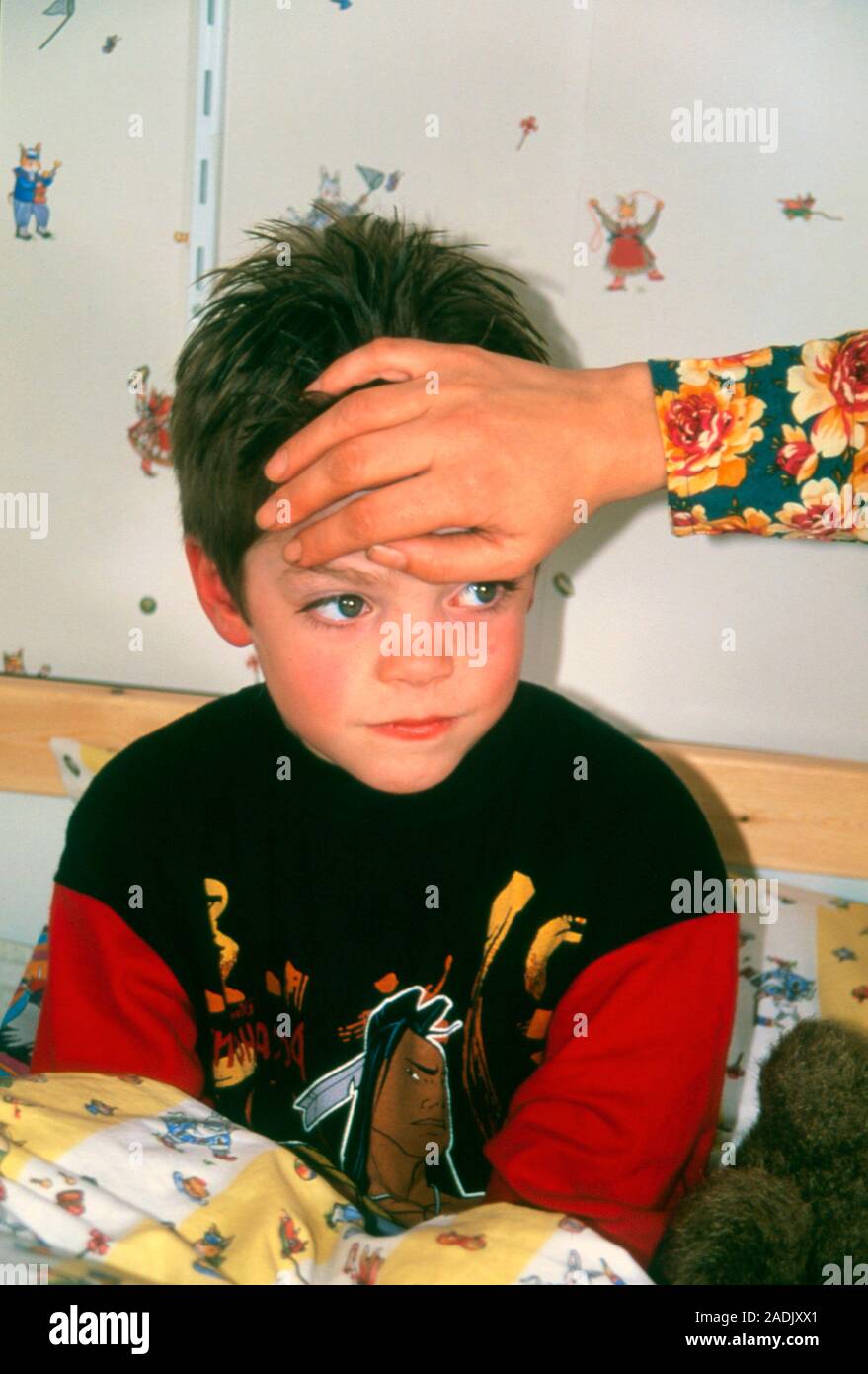 Child with fever. A mother's hand holds the forehead of a six yearold