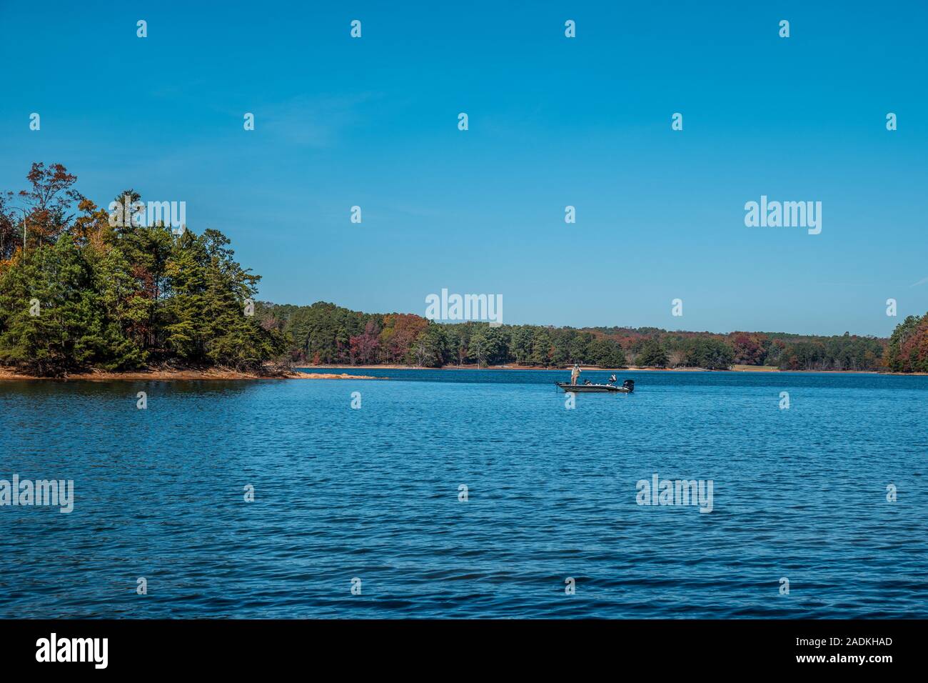 A man fishing on Lake Lanier, Georgia in a motorboat casting a line into the lake off the island shoreline on a vibrant sunny day in autumn Stock Photo