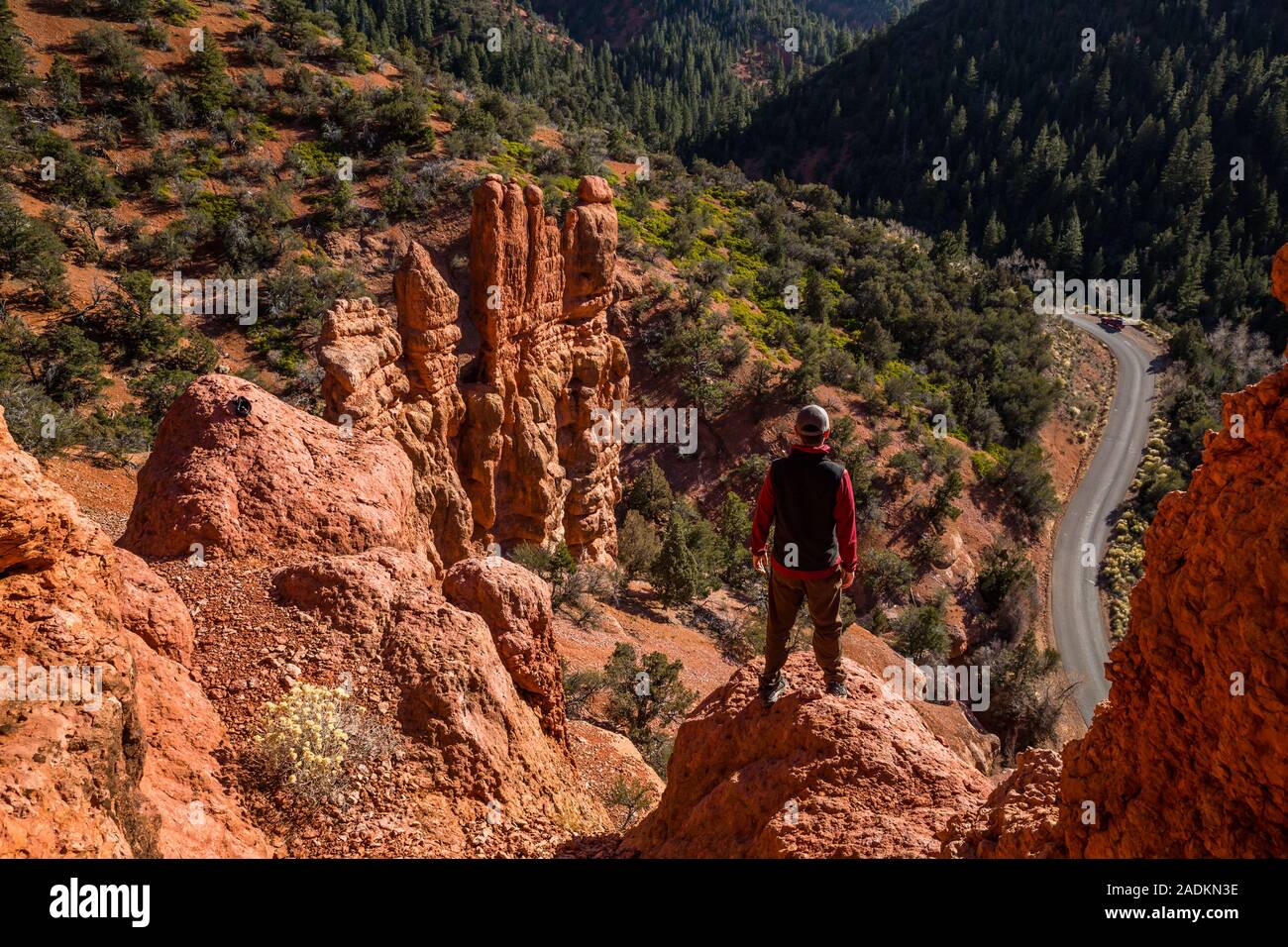 Hiker in sweater and vest standing above roadway in narrow red rock canyon in southern Utah. Stock Photo