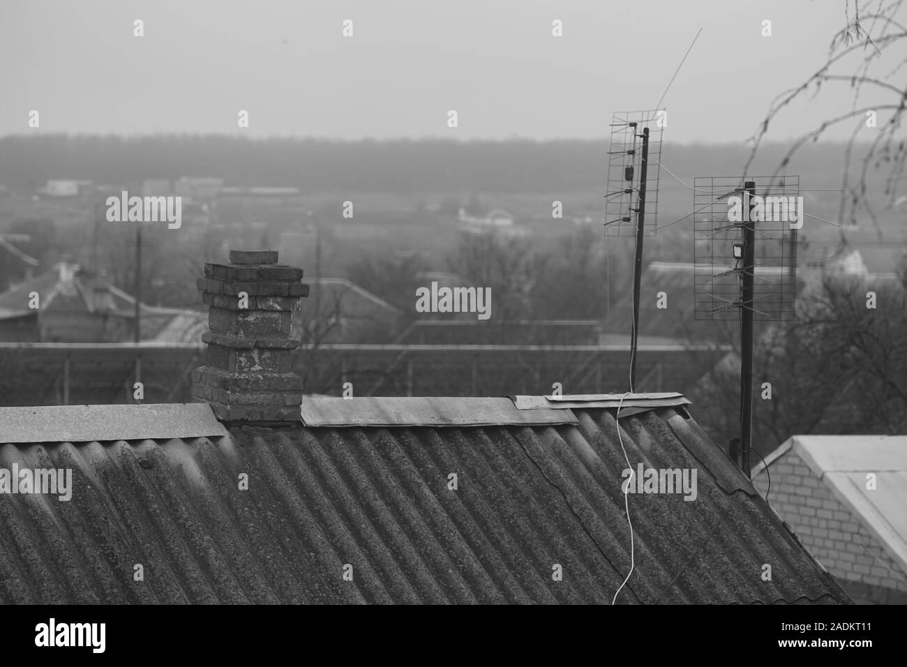 Old rural roof made of corrugated asbestos cement sheet, brick chimney and tv antennas, cloudy day, rural landscape. Stock Photo