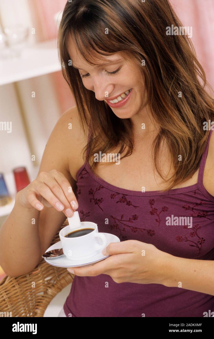 MODEL RELEASED. Adding sugar to coffee. Woman adding a sugar cube to a cup of coffee. Stock Photo