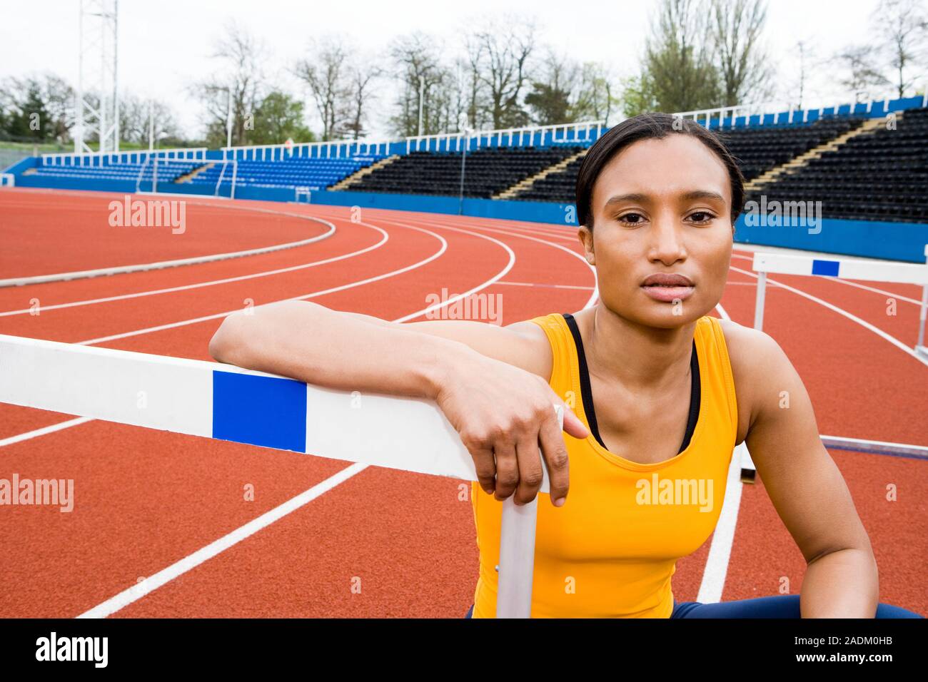MODEL RELEASED. Athlete crouching next to a hurdle on the race track. In athletics hurdling is a