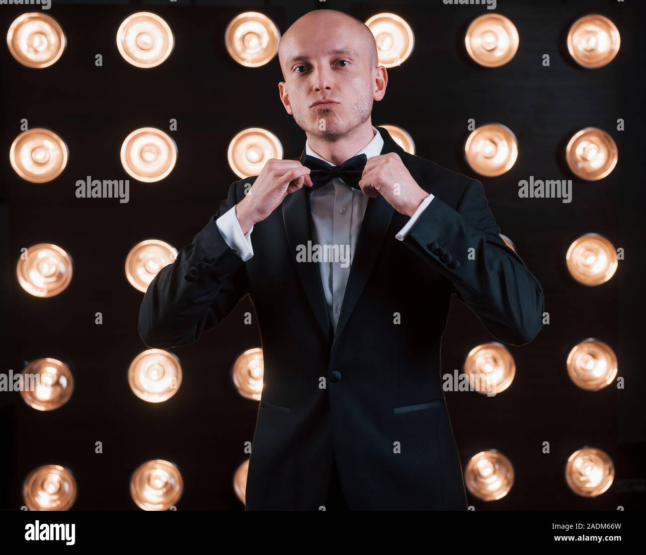 Adjusts the tie. Ready for the show. Magician in black suit standing in the room with special lighting at backstage Stock Photo