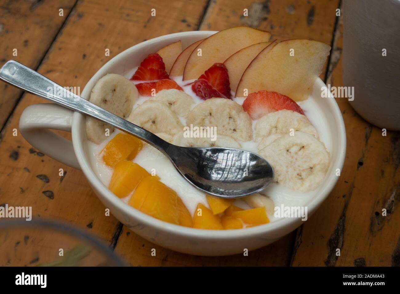 A mug or bowl of fruit ( mango bananas strawberries and apples ) for breakfast in condensed milk Stock Photo