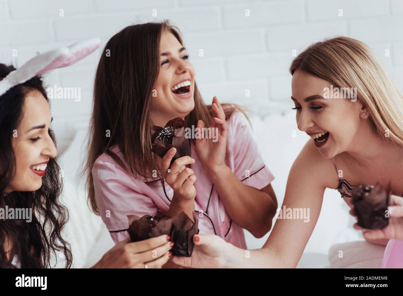 Good joke. Bachelorette party in the bedroom. Delicious looking chocolate cookies at the girlish day. Four women in night wear Stock Photo
