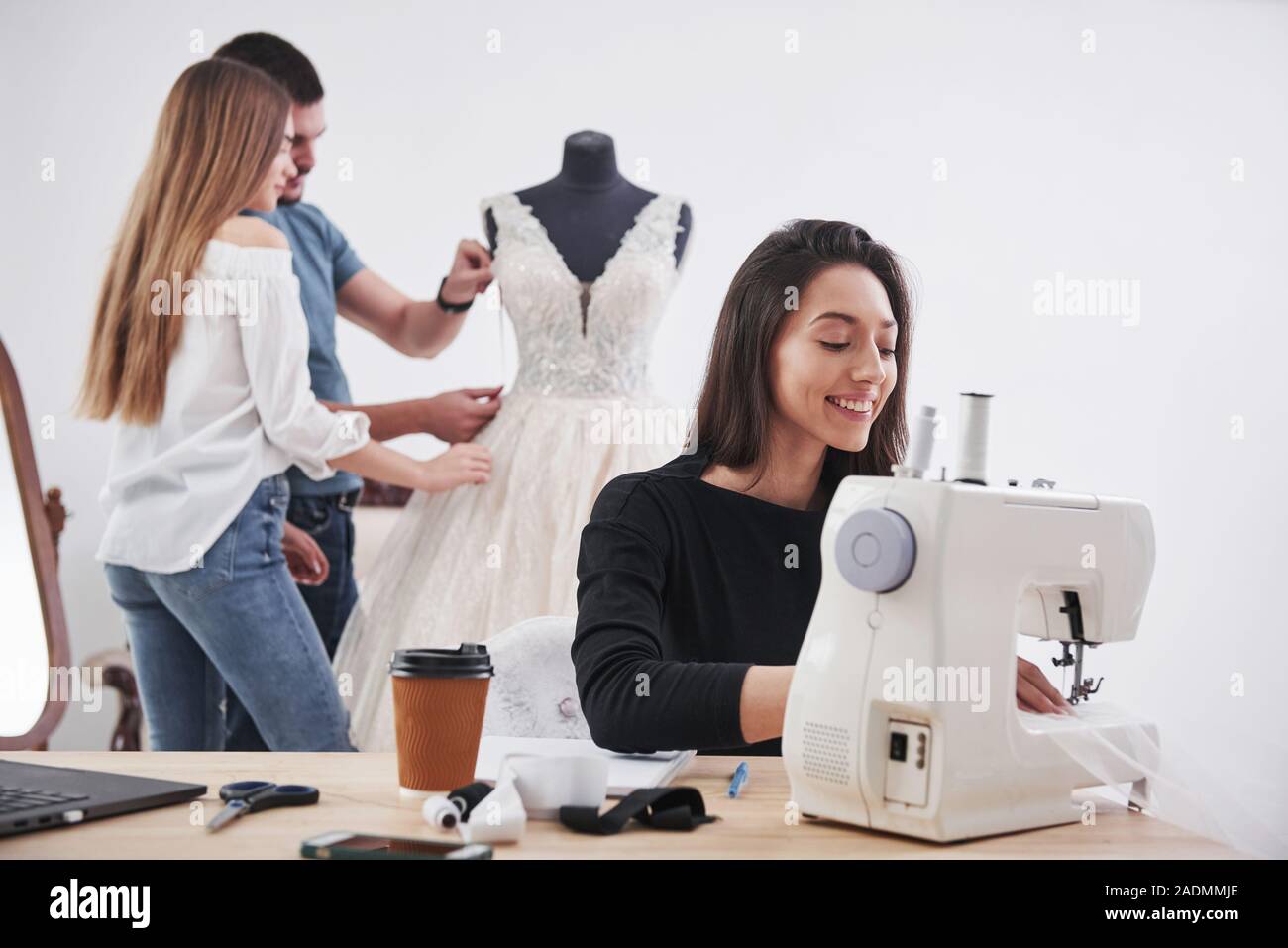 Nice atmosphere. Female fashion designer works on the new clothes in the workshop with group of people behind Stock Photo