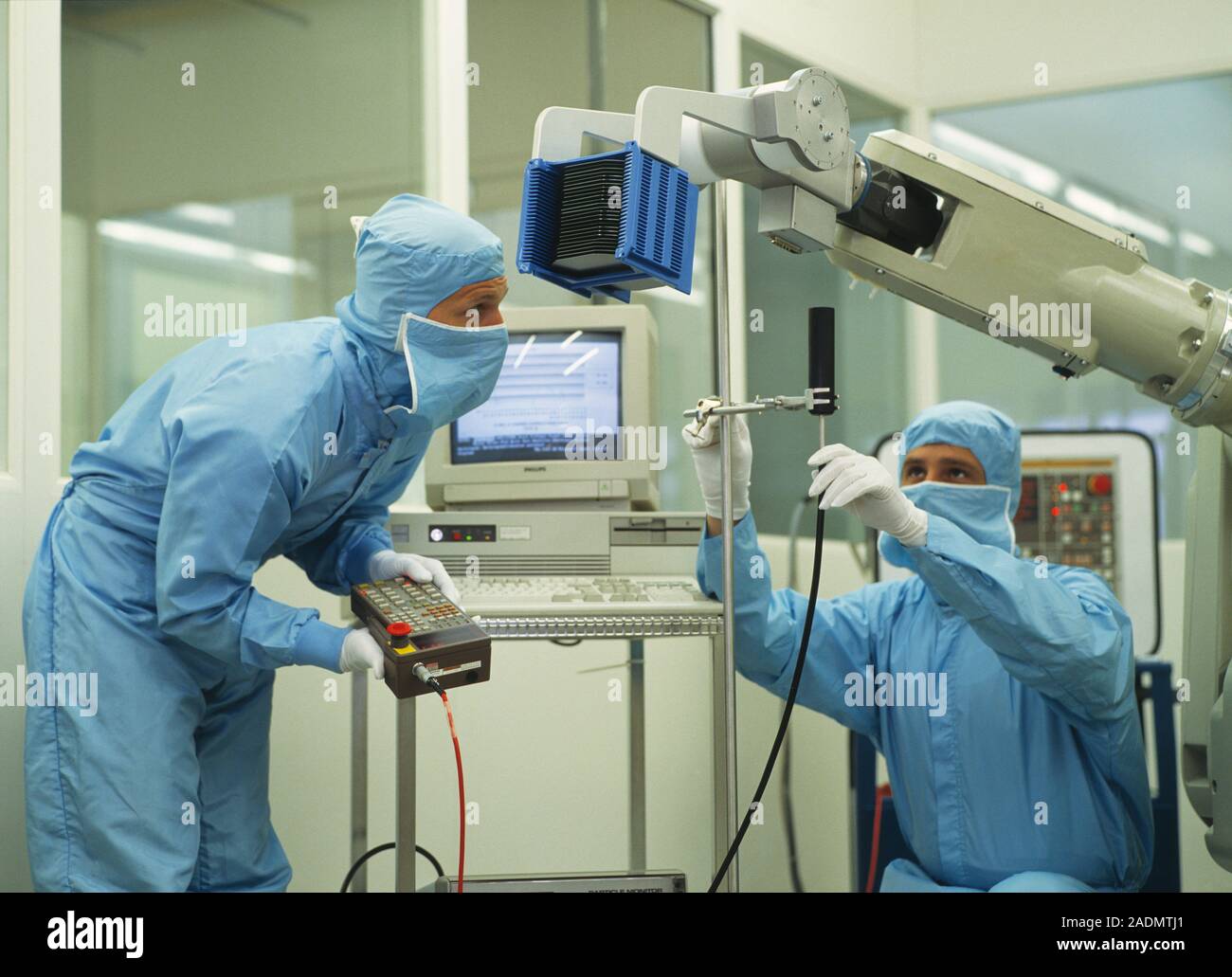 Clean room robot. Technicians programming a robot arm in a clean room ...