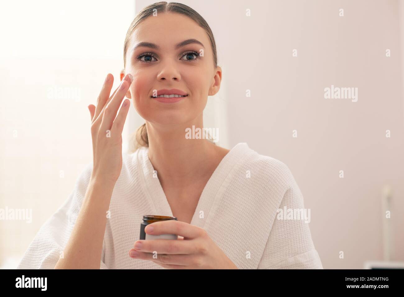 Happy woman smiling while using facial cream Stock Photo