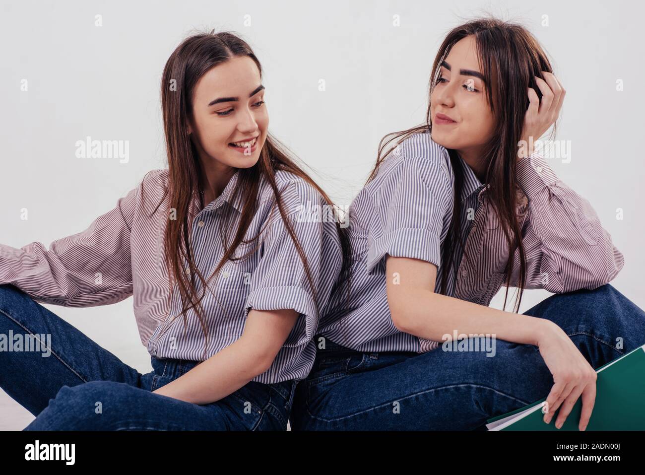 beautiful girls two sisters twins sitting and posing in the studio with white background 2ADN00J