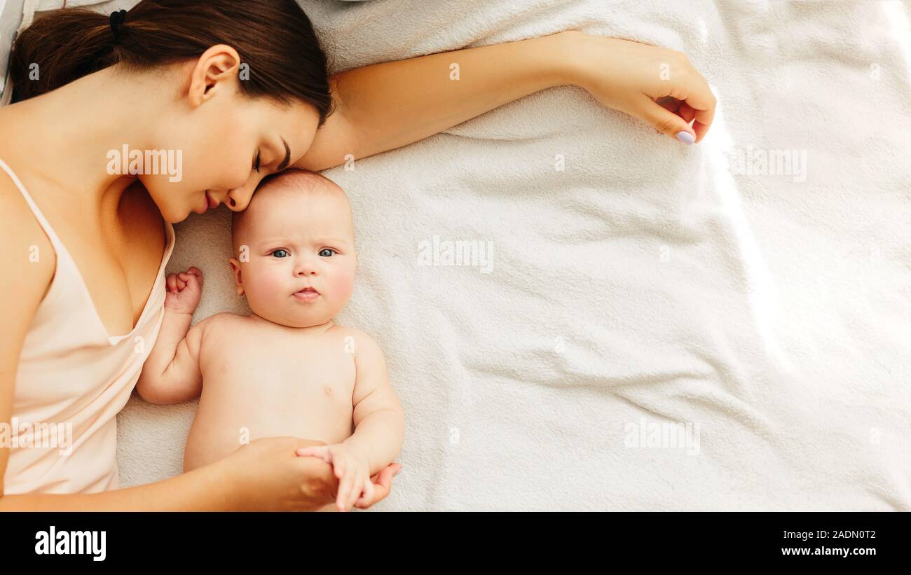 Young beautiful mother lies with the baby on the bed, gently kisses, sleeping together. Stock Photo