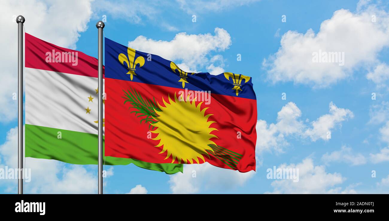 Tajikistan and Guadeloupe flag waving in the wind against white cloudy blue sky together. Diplomacy concept, international relations. Stock Photo