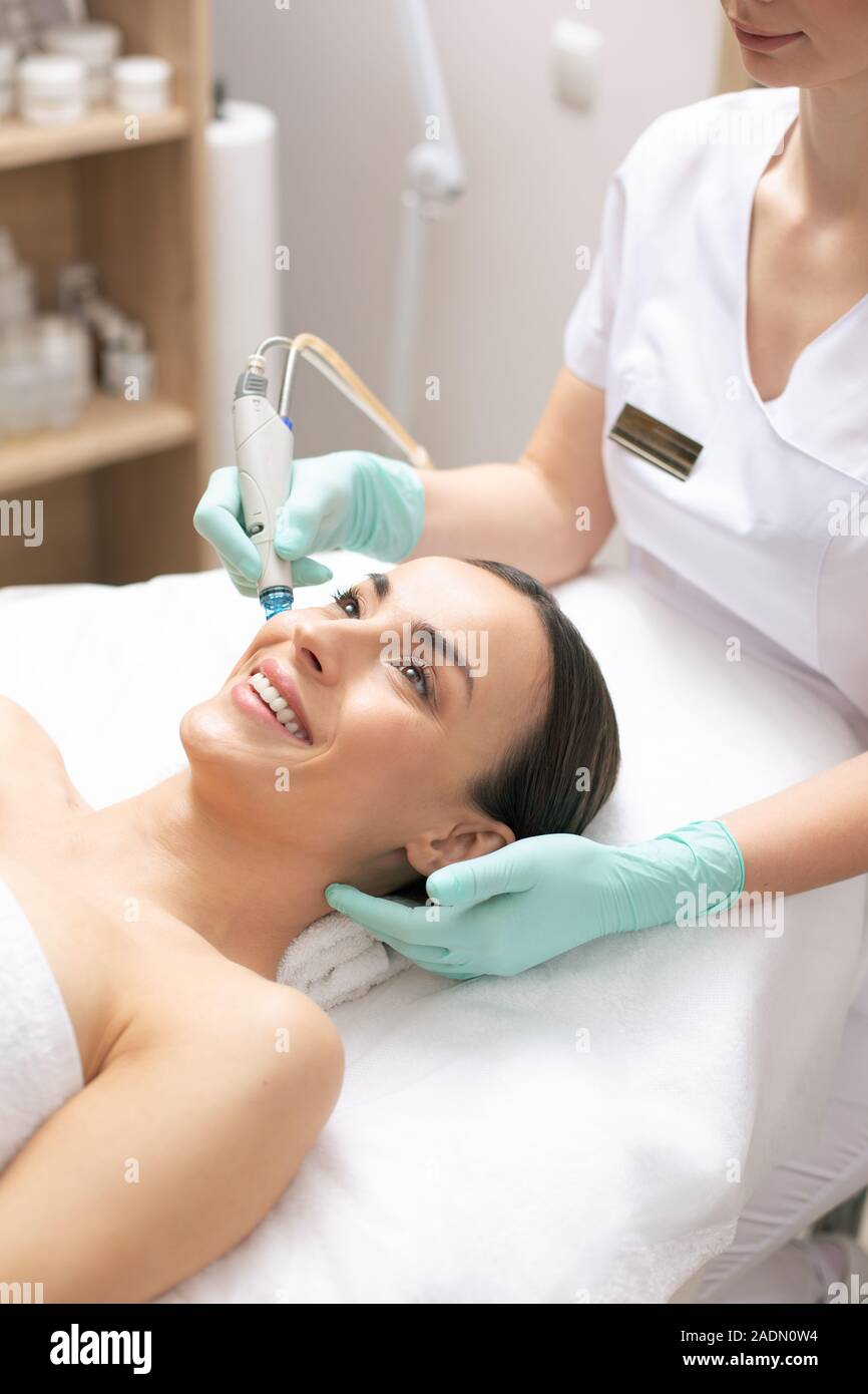 Careful cosmetologist working in rubber gloves while holding tool Stock Photo