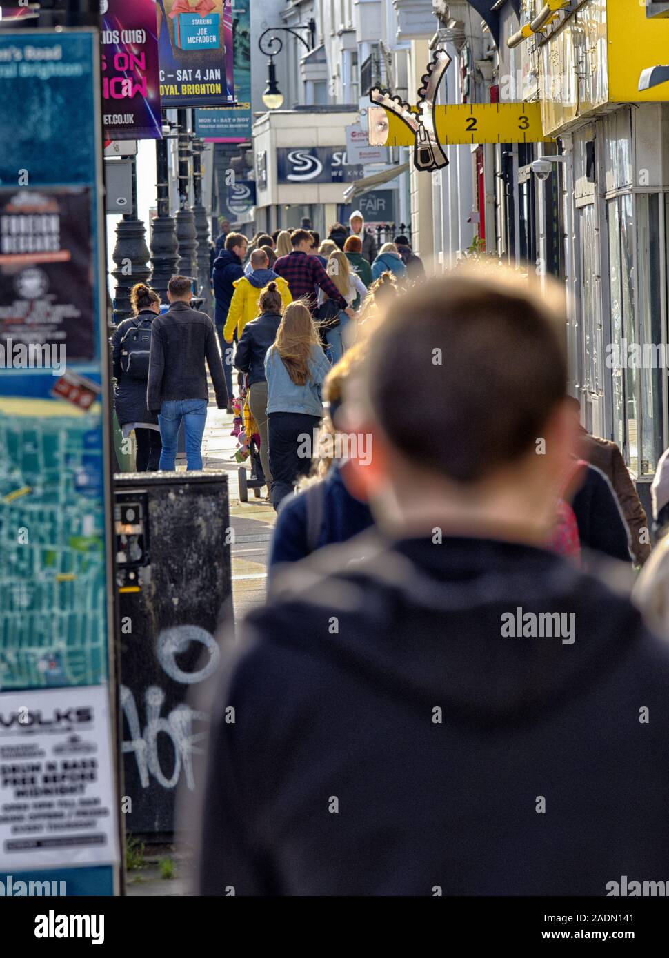 Crowds of busy shoppers, rush hecticly down Brighton's Queen's Road, surrounded by posters, flyers and advertisement hoardings. Stock Photo