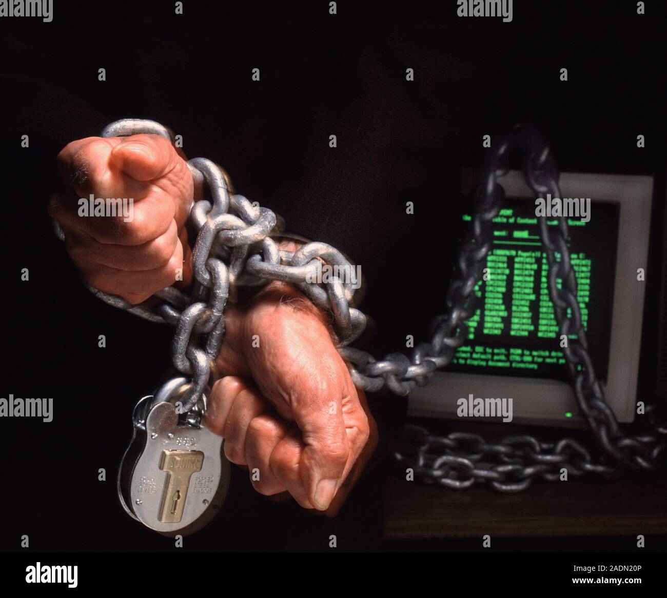 Computer dependency. Conceptual image of a pair of hands chained to a computer screen. This image may represent an addiction to internet use, or socie Stock Photo