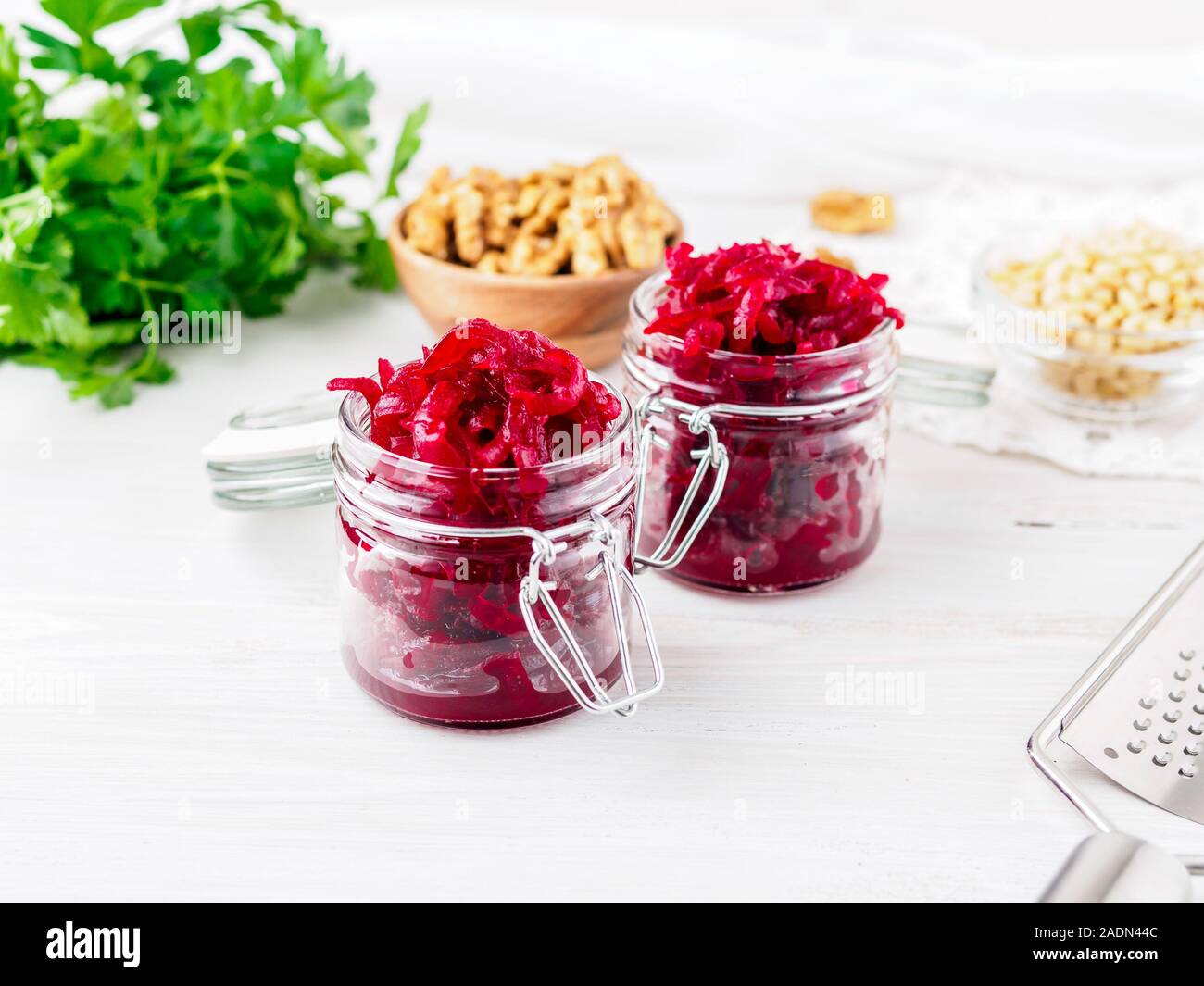 Fresh salad of grated boiled beetroot in glass jars, white wooden background, side view. Stock Photo