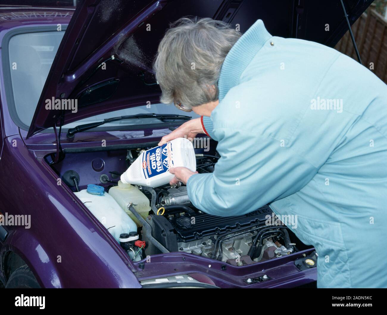 Antifreeze and car engine. Elderly lady pouring antifreeze into a car's