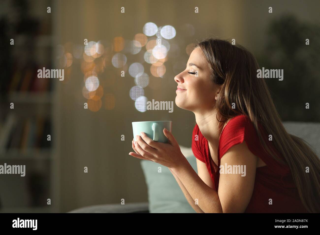 Side view portrait of a relaxed woman drinking coffee sitting on a couch in the night at home Stock Photo